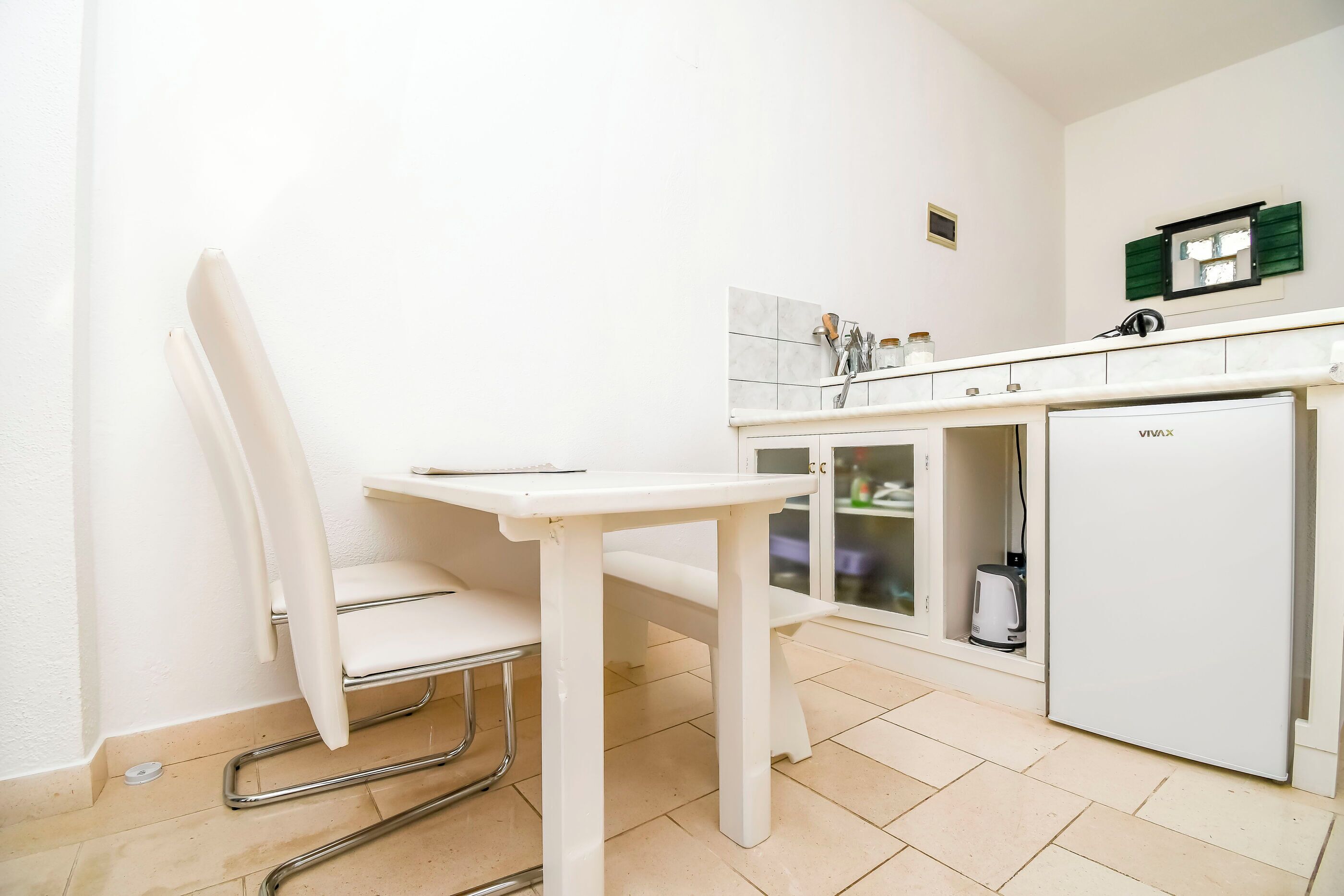 A small kitchenette with a white table, a chair, a sink, and a refrigerator.