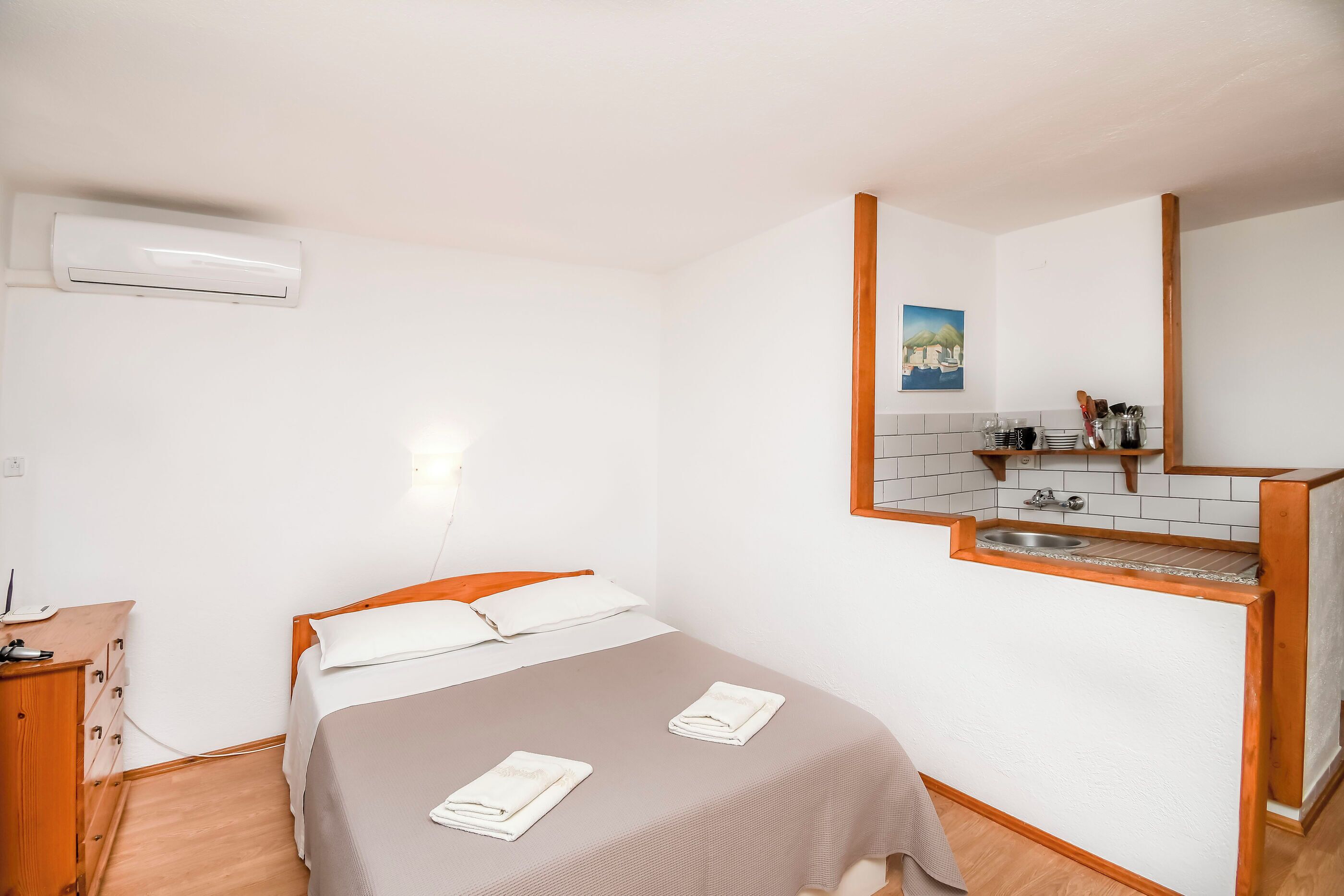 Een slaapkamer met een bed, een houten dressoir, een klein wastafeltje en een spiegel.