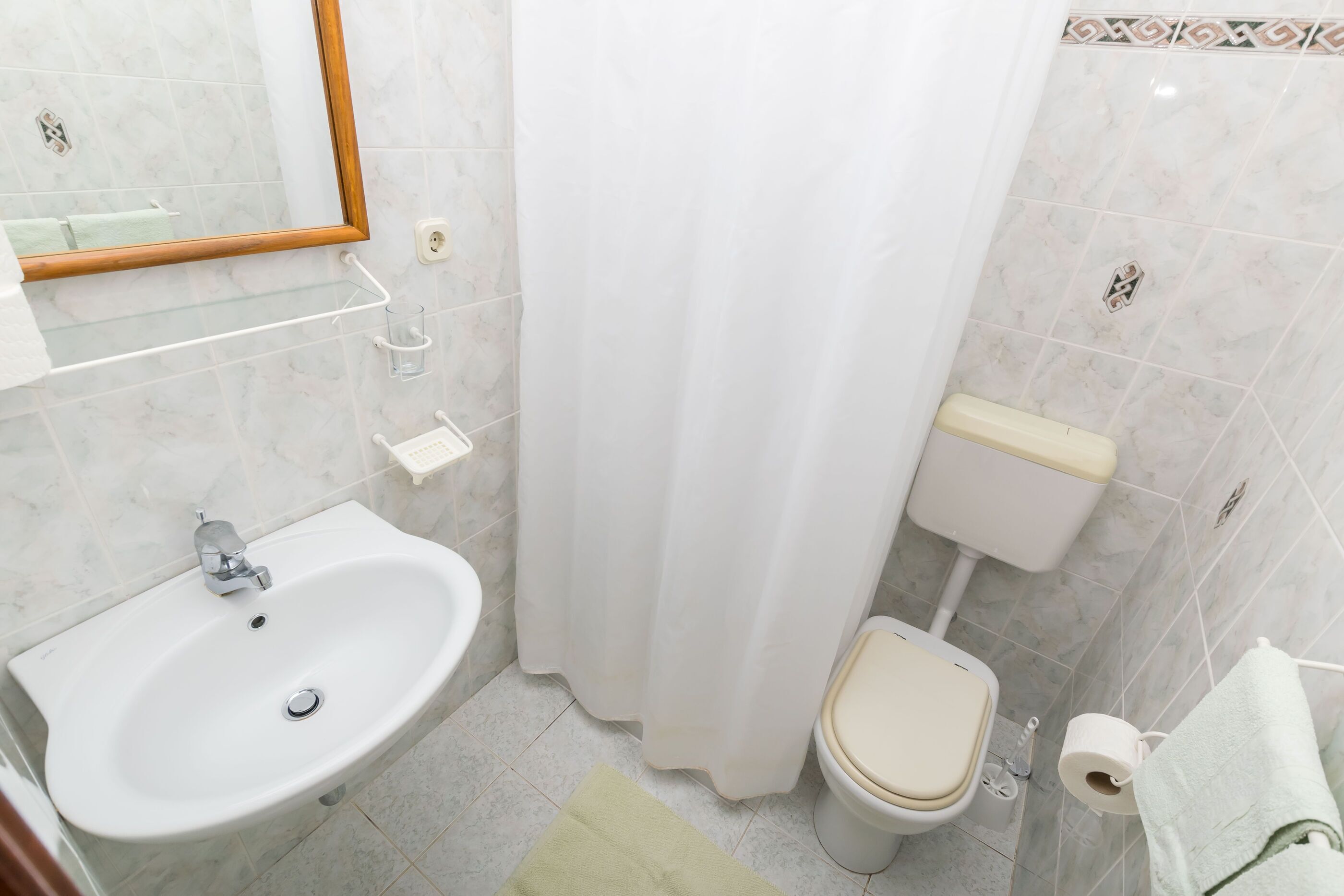 Egy fürdőszoba, amelyben mosdókagyló, WC és zuhanyfüggöny található.