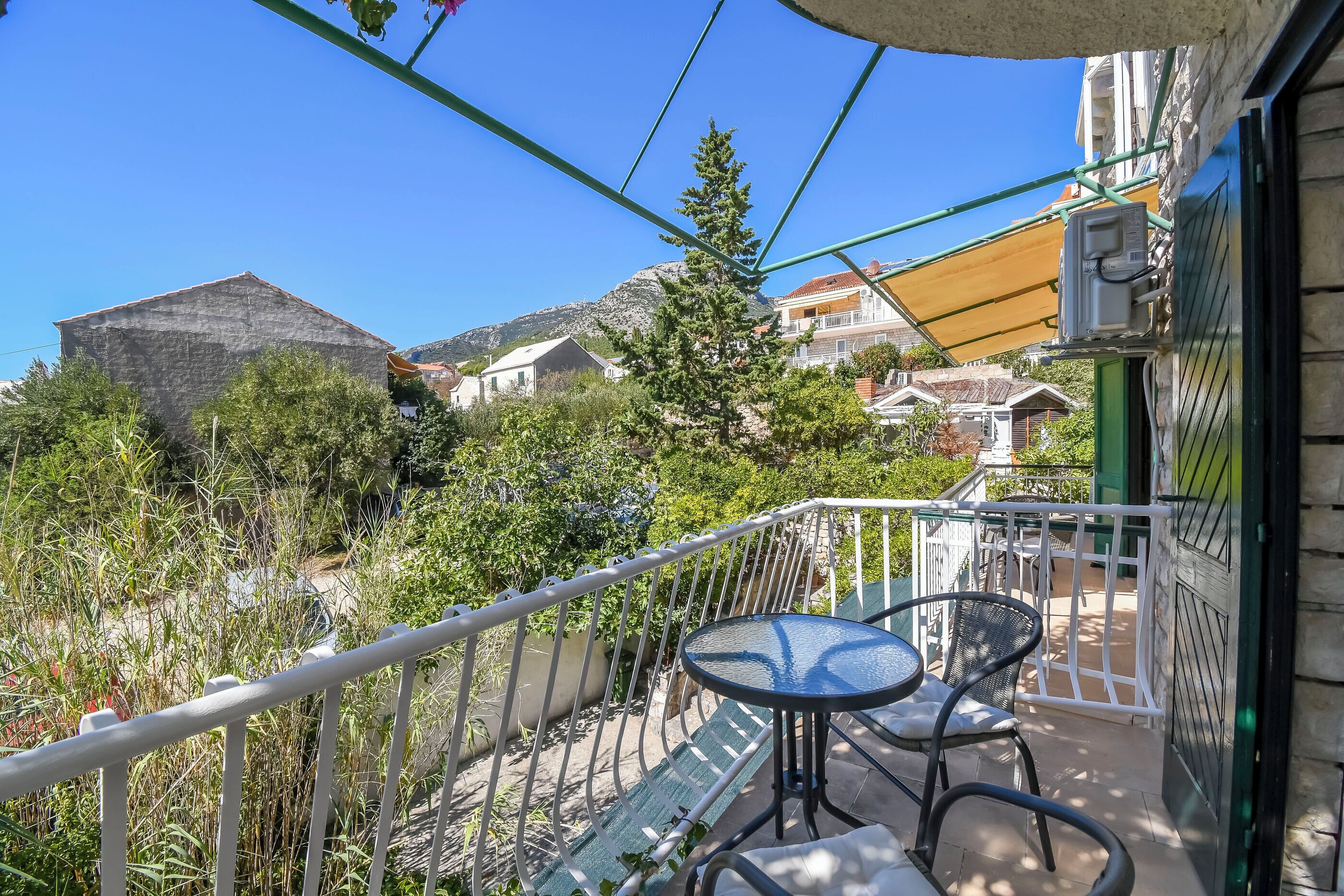 A balcony with a table and chairs, a railing, and a view of buildings and trees.