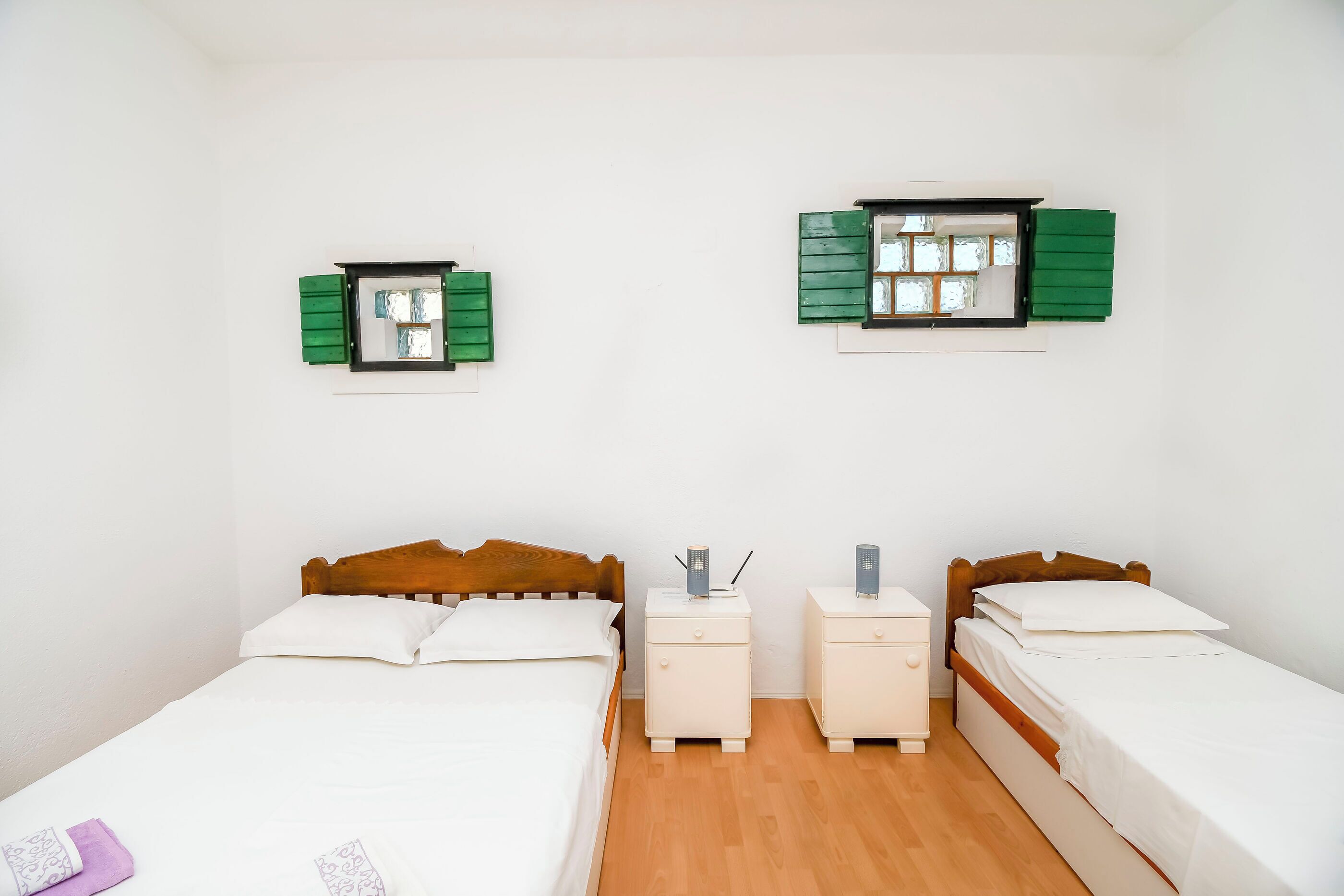 Une chambre double avec deux lits simples, une petite table de chevet avec une lampe et un miroir mural avec des volets.