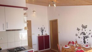 A compact kitchen with white cabinets, a red dining area with a table set for two, and a wooden ceiling. - Apartments Sto (Hvar)