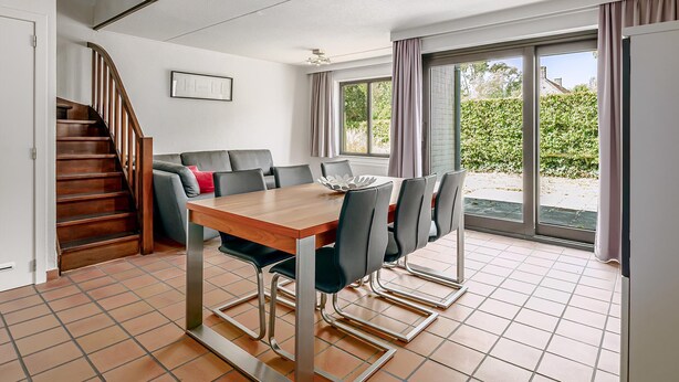 A dining area with a wooden table and chairs, a staircase, and a view of greenery through large windows. - 3 bedroom accommodation in Nieuwpoort (Nieuwpoort)