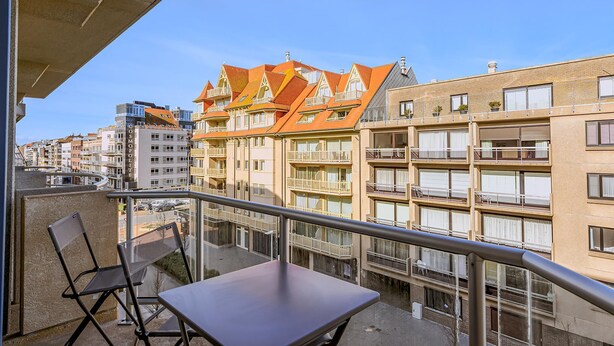A balcony with a table and chairs, overlooking a row of buildings with orange roofs and balconies.