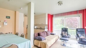 Ein modernes Wohnzimmer mit einer Couch, zwei Sesseln, einem Glastisch und einem Esstisch.