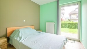 Ein Schlafzimmer mit einem Bett, einem Nachttisch, einer Heizung und einer Schiebeglastür zum Garten.