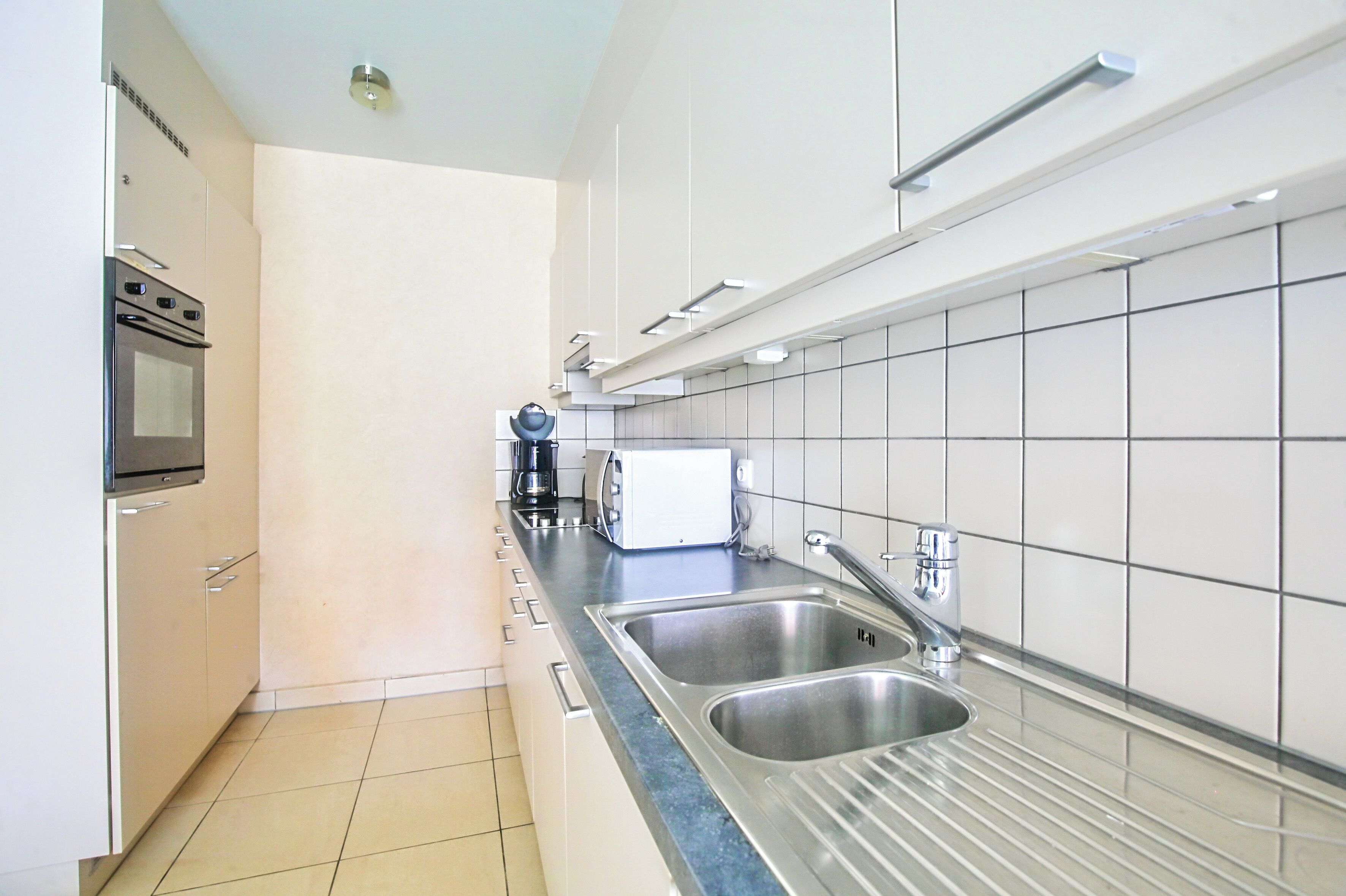 A modern kitchen with stainless steel appliances, a double sink, and white tiled walls.