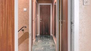 A narrow hallway with a wooden door at the end, a light switch on the wall, and a black security camera. - 5 bedroom accommodation in Koksijde (Koksijde)