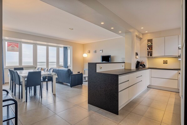 A modern kitchen with white cabinets, a central island, and a dining area with a table and chairs.