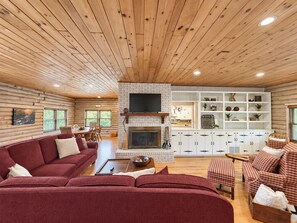 Interno di una baita in legno con camino, soffitto in legno e un angolo salotto accogliente.