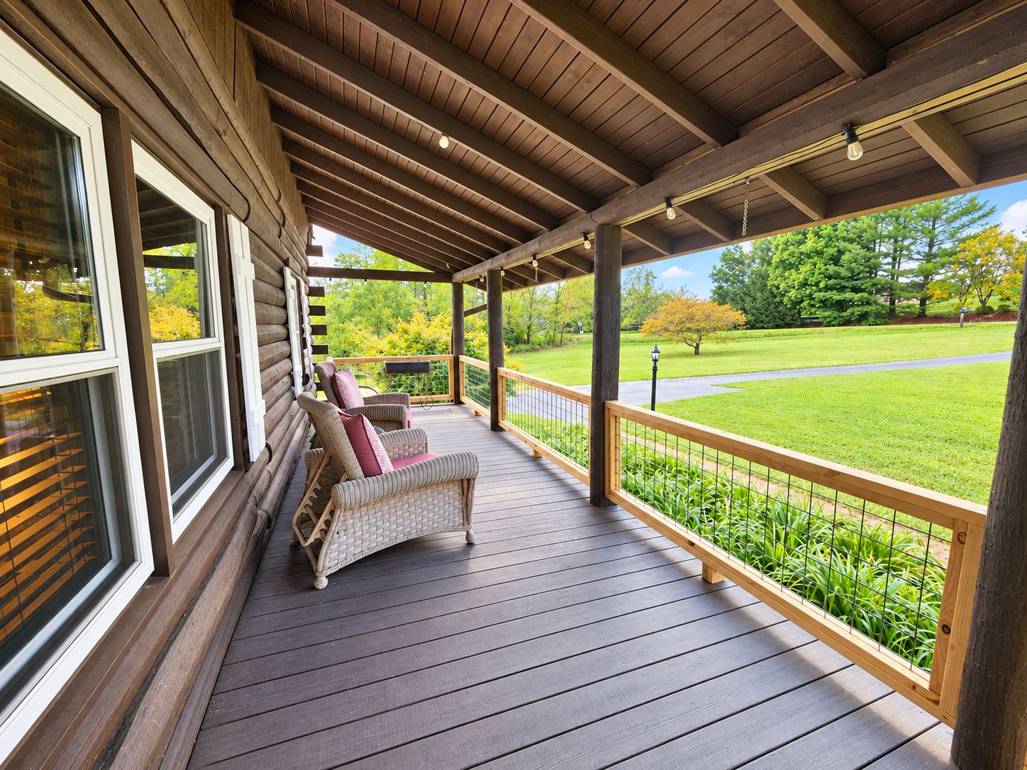 A covered porch with a wooden deck, wicker chairs, and a view of a green landscape.