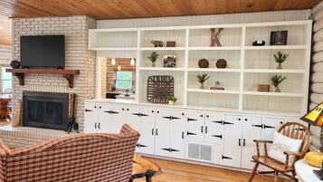 A cozy living room with a fireplace, wooden ceiling, and a white entertainment unit with shelves.