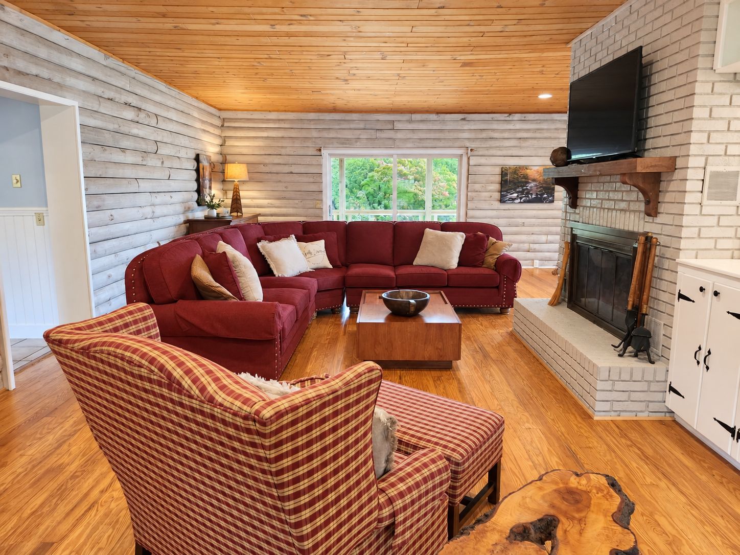 A log cabin interior with a sectional sofa, a plaid armchair, a wooden coffee table, and a fireplace.
