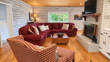 A log cabin interior with a sectional sofa, a plaid armchair, a wooden coffee table, and a fireplace.