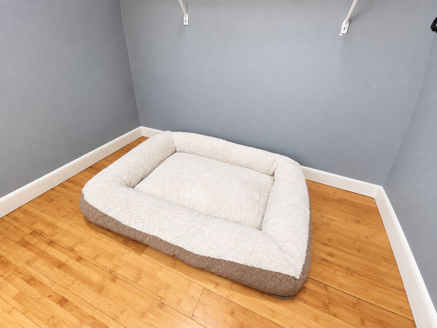 A pet bed in a corner of a room with wooden flooring and light blue walls.