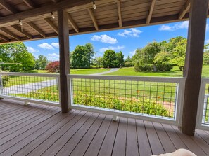 Ein überdachter Außenbereich mit Holzdeck, Metallgeländer und Blick auf einen angelegten Garten mit Bäumen und einem Weg.