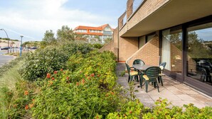 A patio area with a table and chairs, surrounded by greenery and a brick building. - ZeeZonZand A-GV01 + P* (Koksijde)