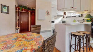 A compact kitchen with a central island, a dining area with a patterned tablecloth, and a small bar area with stools. - ZeeZonZand A-GV01 + P* (Koksijde)