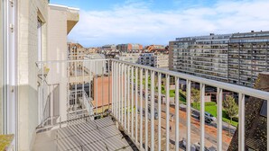 Un balcon doté d’une balustrade en métal, d’où l’on peut admirer un paysage urbain composé de nombreux bâtiments et d’un ciel dégagé.