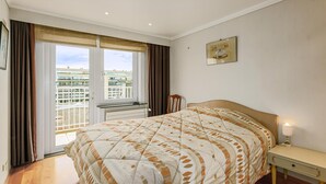 Une chambre d’hôtel avec un lit, une table de chevet, une fenêtre avec des rideaux, un tableau accroché au mur et une vue sur un bâtiment à l’extérieur.