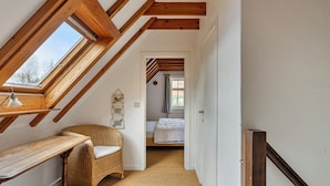 A narrow hallway with a sloped ceiling, a wicker chair, a desk, and a bed in the background.