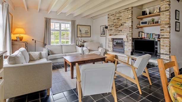 A cozy living room with a fireplace, white sofas, and a stone wall.