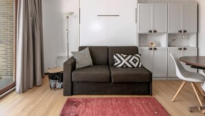 Una sala de estar moderna con un sofá gris, un tapete rojo, una mesa de comedor y un armario blanco.