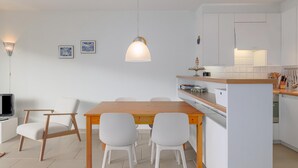 Una cocina moderna con armarios blancos, una isla de madera y una zona de comedor con mesa de madera y sillas blancas.