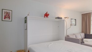 Un dormitorio ordenado con una cama, una mesita de noche, una lámpara y un pequeño estante con adornos.