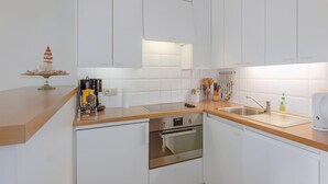 Una cocina moderna con armarios blancos, un horno de acero inoxidable, un lavamanos y una encimera con diversos utensilios de cocina.