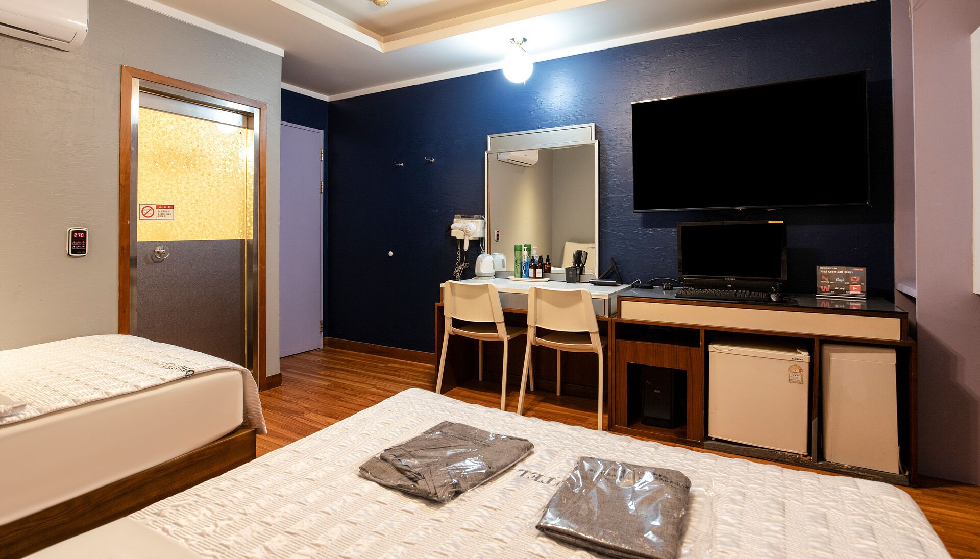 A hotel room with a bed, a desk, a chair, a TV, and a small refrigerator.