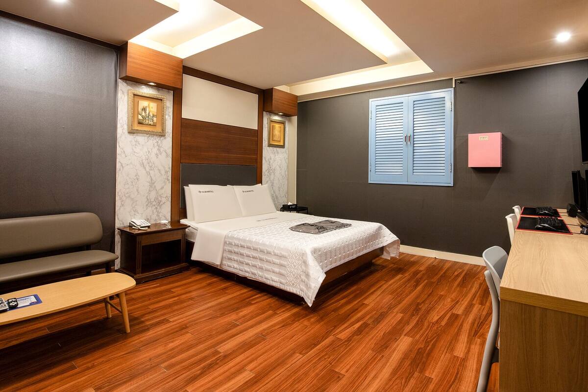 A hotel room with a bed, a desk, a chair, a sofa, and a TV.