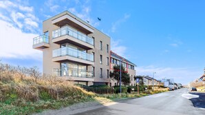 A modern multi-story building with balconies, a clear sky, and a road in the foreground.
