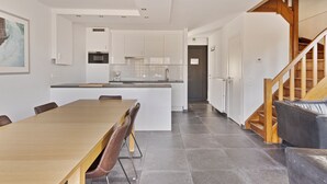 Eine moderne Küche mit weißen Schränken, einer zentralen Kochinsel und einem Essbereich mit einem langen Tisch und Stühlen.