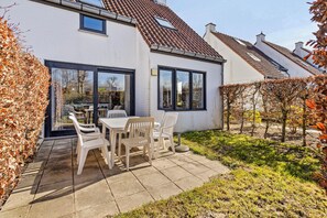 Ein modernes Haus mit Terrasse, einem Esstisch mit Stühlen und einem Garten.