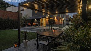 A covered outdoor dining area with a table and chairs, a barbecue grill, and a patio with a view of a modern house. - New Villa next to the forest and Therme SPA (Corbeanca)