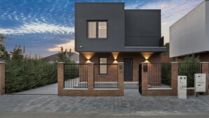 A modern two-story house with a dark facade, a visible window, and a gated entrance. - New Villa next to the forest and Therme SPA (Corbeanca)