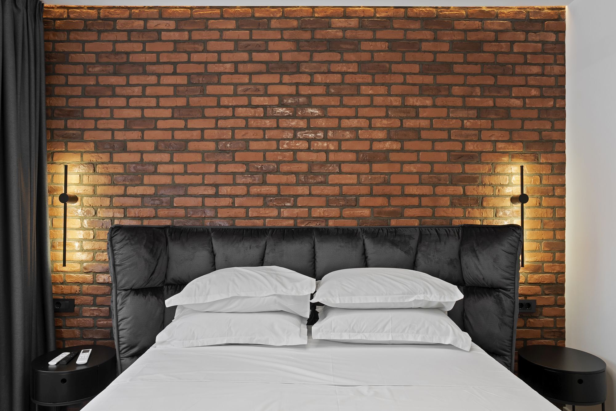 A bed with a black headboard, white bedding, and two bedside tables with remote controls.
