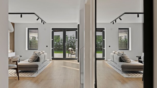 A modern living room with a sofa, a coffee table, and a dining area with chairs. There are large windows providing natural light and a view of the outdoors. - New Villa next to the forest and Therme SPA (Corbeanca)