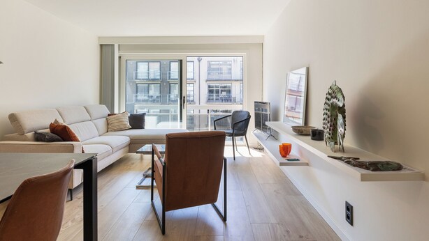 Una sala de estar moderna con sofá, mesa de comedor, sillas y un ventanal con vistas a la ciudad.