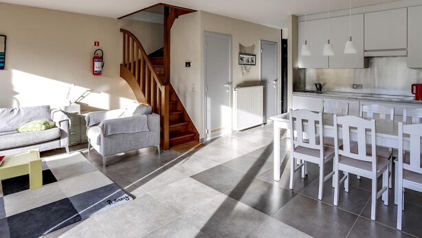 Una cocina moderna con armarios blancos, un comedor con sillas blancas y una escalera que lleva a otro nivel.