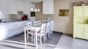 Una cocina moderna con armarios blancos, una mesa de comedor con sillas y un mueble amarillo.