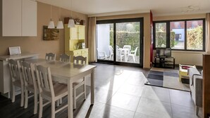 Una cocina moderna con comedor, grandes puertas correderas de vidrio hacia un patio y un televisor en la sala.