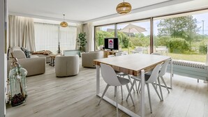 A modern living room with a wooden dining table, white chairs, a sofa, and a TV. - 2 bedroom accommodation in De Panne (De Panne)