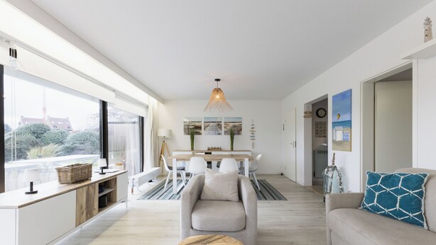 A modern living room with a sofa, a wooden coffee table, and a dining area with a table and chairs. - 2 bedroom accommodation in De Panne (De Panne)