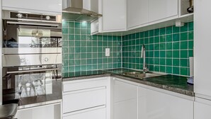 A modern kitchen with white cabinets, a green tiled backsplash, stainless steel appliances, and a sink. - 2 bedroom accommodation in De Panne (De Panne)