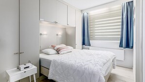 A bedroom with a bed, bedside table, and a window with curtains. - 2 bedroom accommodation in De Panne (De Panne)