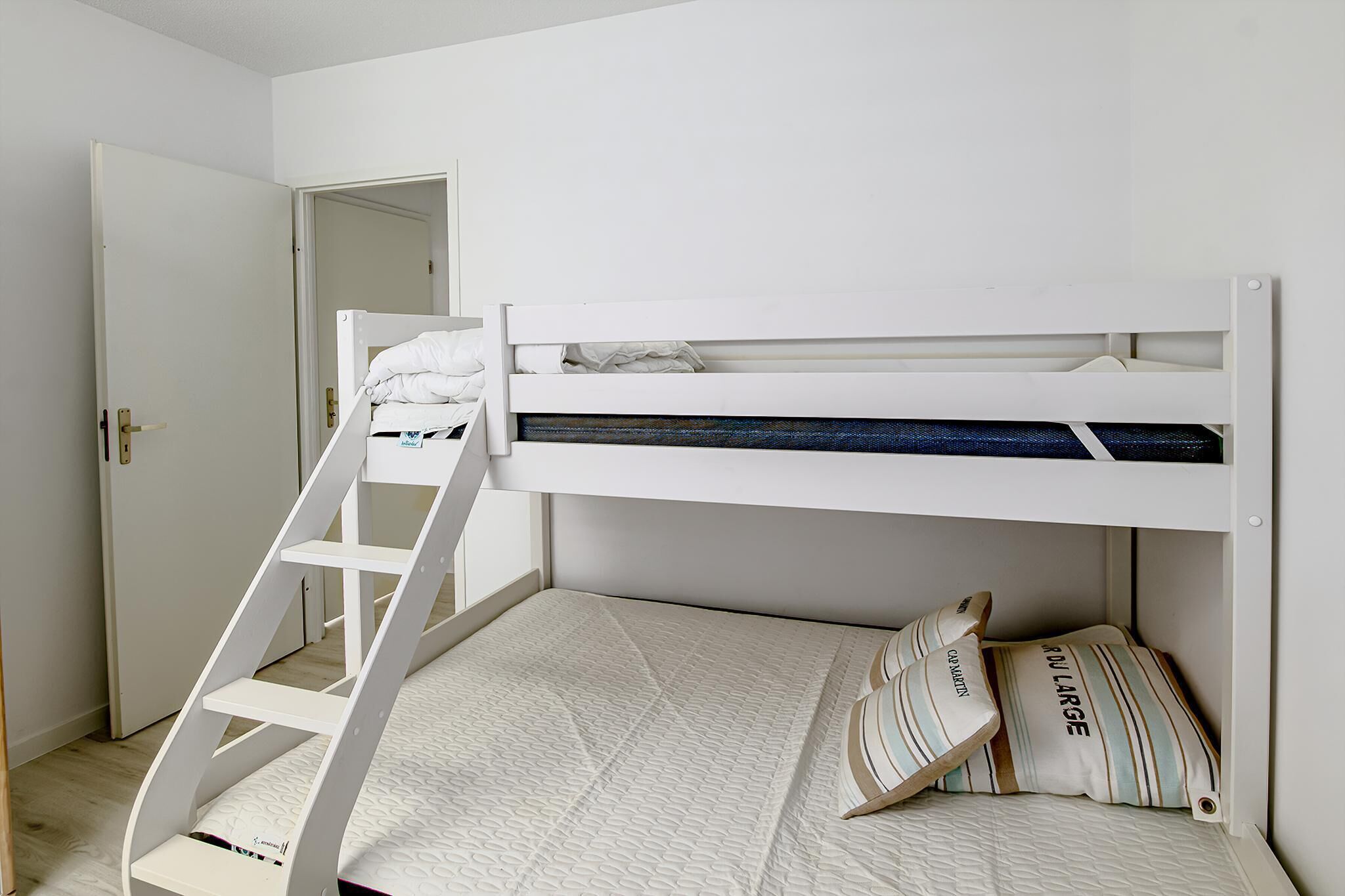 Een stapelbed met een ladder, een deur en een matras met kussens.