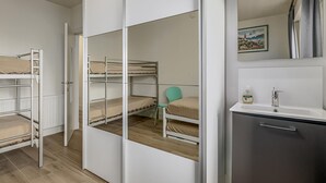 A bedroom with bunk beds, a small chair, a mirror, and a bathroom with a sink and cabinet. - 2 bedroom accommodation in De Panne (De Panne)