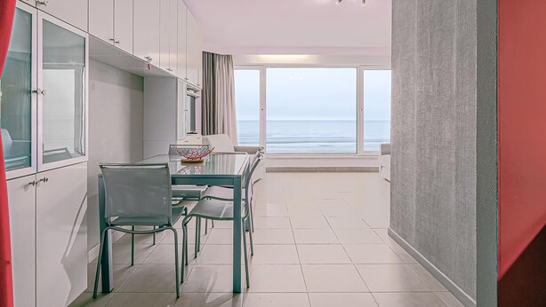 A modern kitchen with white cabinets and a dining area with a glass table and chairs. - 1 bedroom accommodation in Sint Idesbald (Sint Idesbald)